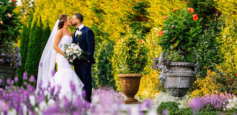 Bride holding her wedding bouquet while kissing the groom in the venues garden.