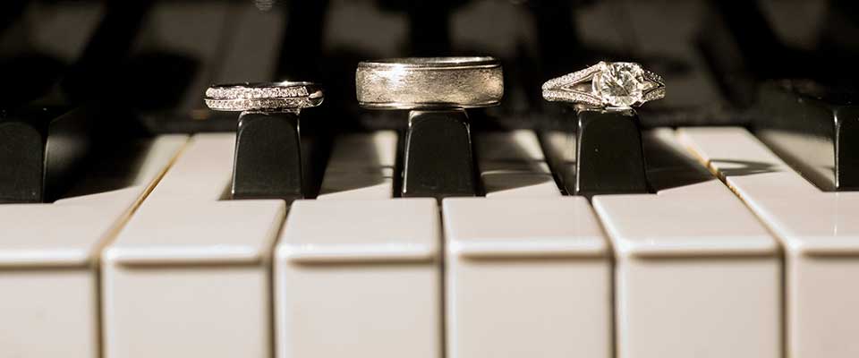 Piano keys with engagement ring and wedding bands placed on top of black keys.