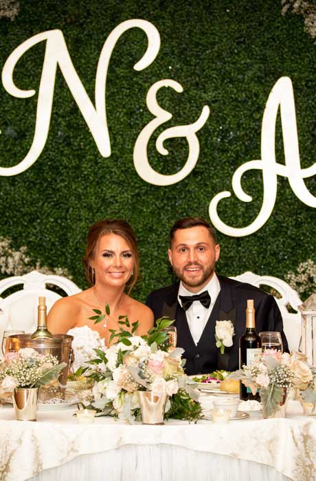 Bride and Groom sitting at their bridal table in front of their monogram flower wall behind them.