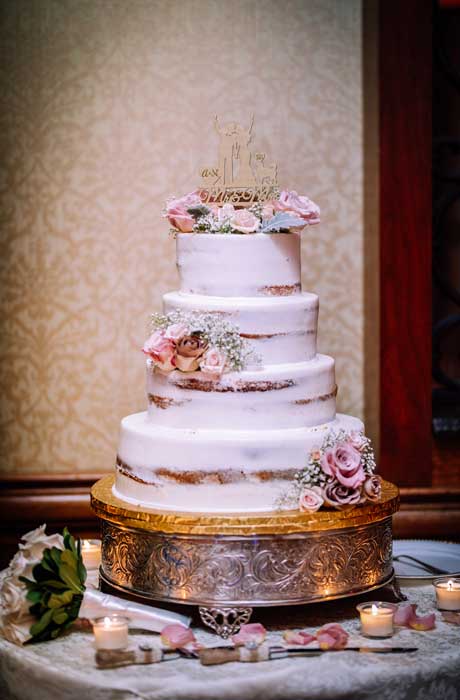 A four-tier wedding cake with flowers placed on each tier.
