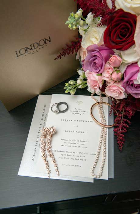 Brides wedding jewelry on top of her wedding invitation next to a London Jewelers gold bag. 
