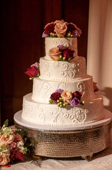 Four tied white wedding cake with red and peach flower on each tier. 