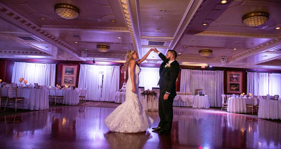 Bride and Groom in their purple up lighting reception room holding hands. 
