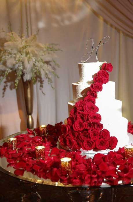 . White wedding cake with red roses cascading down the side of the cake surrounded with red rose pet