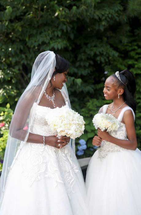 Bride with daughter both in white gowns holding white bouquets.