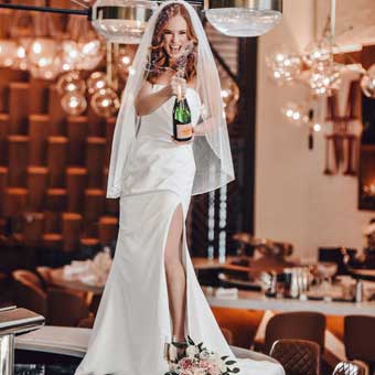 Bride standing on bar holding champagne bottle. 