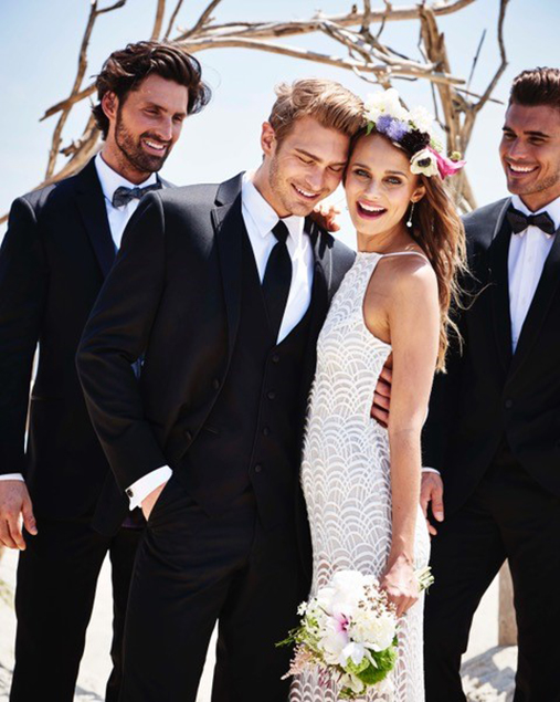 One Groom and Two Groomsmen in Black Tuxedos standing next to Bride with Bouquet.