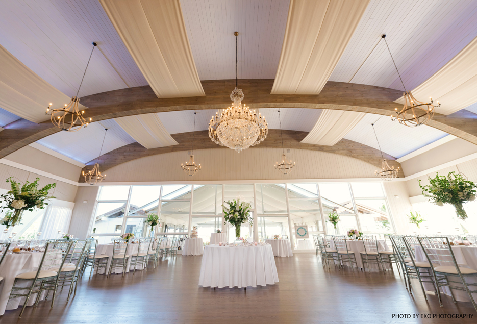 A view of white tables for the guests with flowers and various chandeliers.
