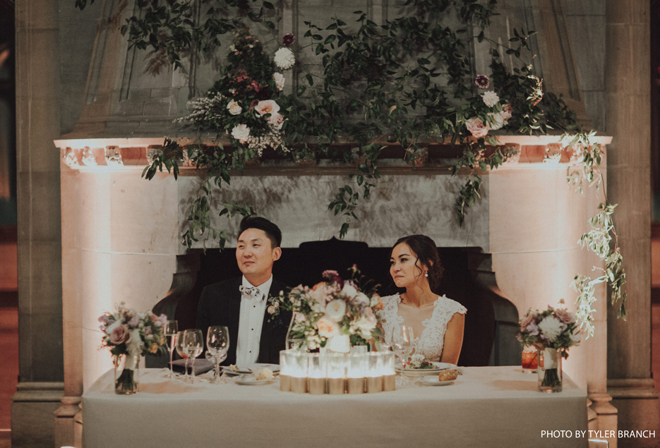 Bride and groom sitting at their reception table surrounded by flowers.