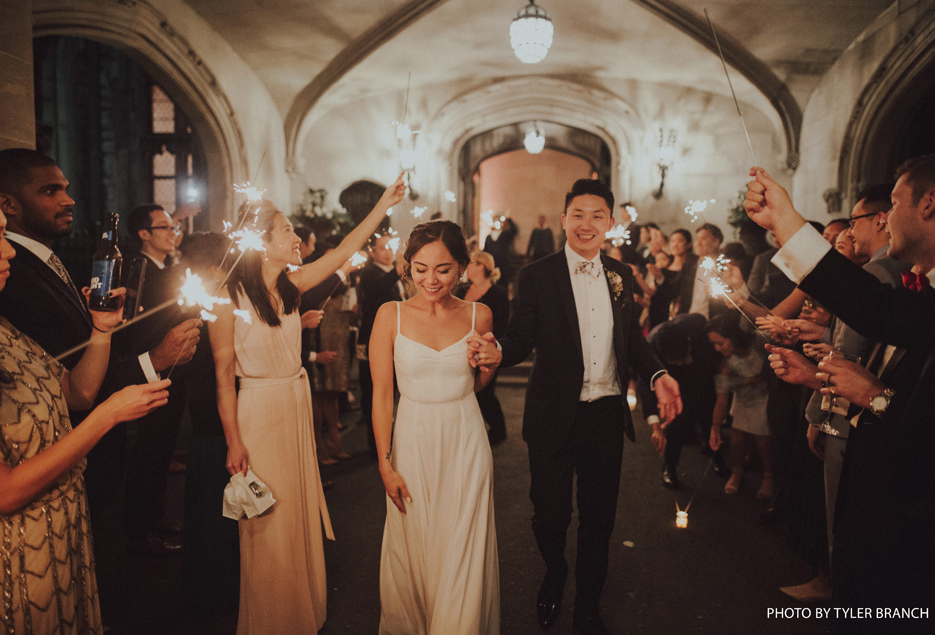 Bride and groom walk through guests holding sparklers. 