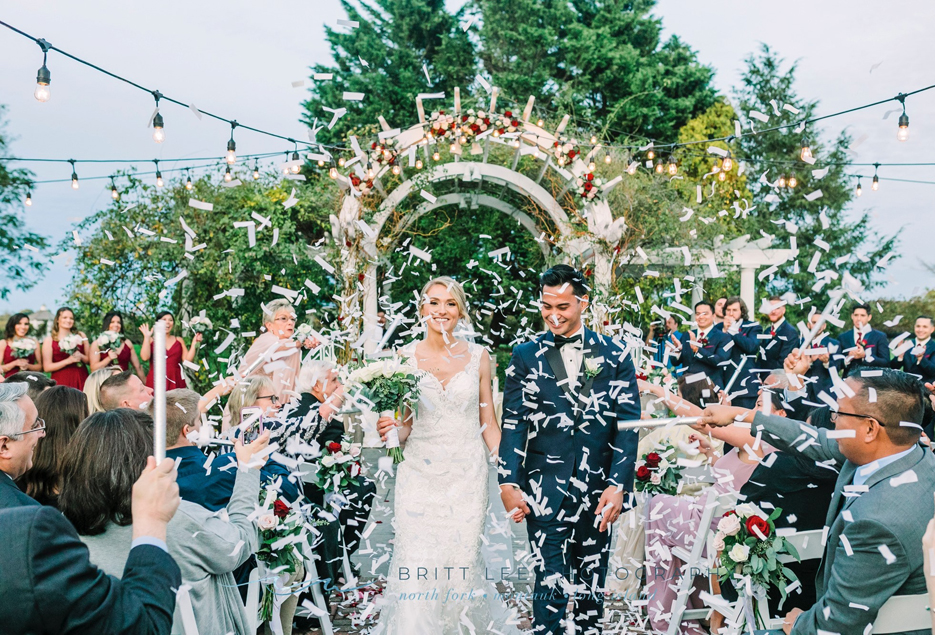 Bride and groom walk down the aisle while guests throw confetti.