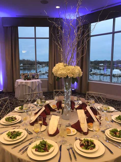 Wedding reception table set up, with tall centerpiece containing white flowers. 