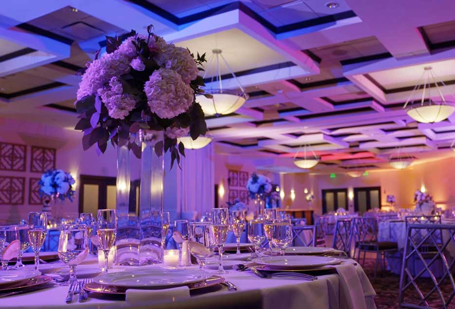 Ballroom setup with tall flower centerpieces with purple uplighting. 
