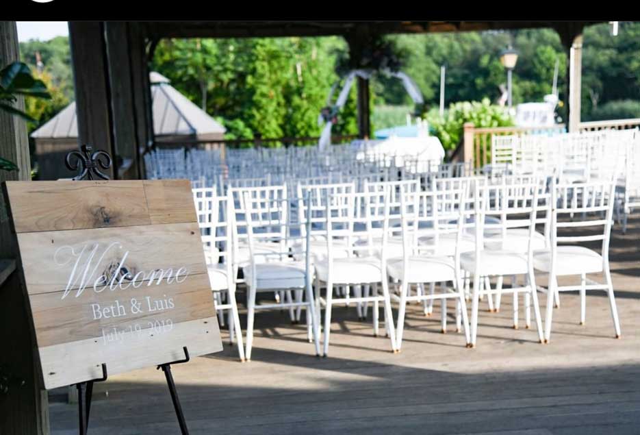 A outdoor ceremony setup with white chairs and a welcome board for the guest. 