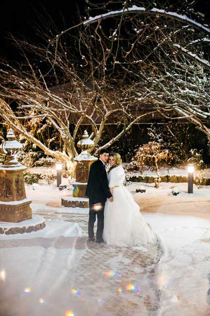 The bride and groom posing outside  with snow as their background.