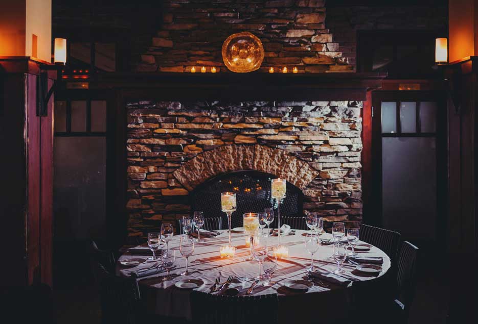 A closeup shot of a large table setup next to a warm fireplace. 