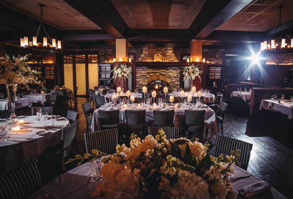 Full room shot of an event setup with tall flower centerpieces  on the tables. 