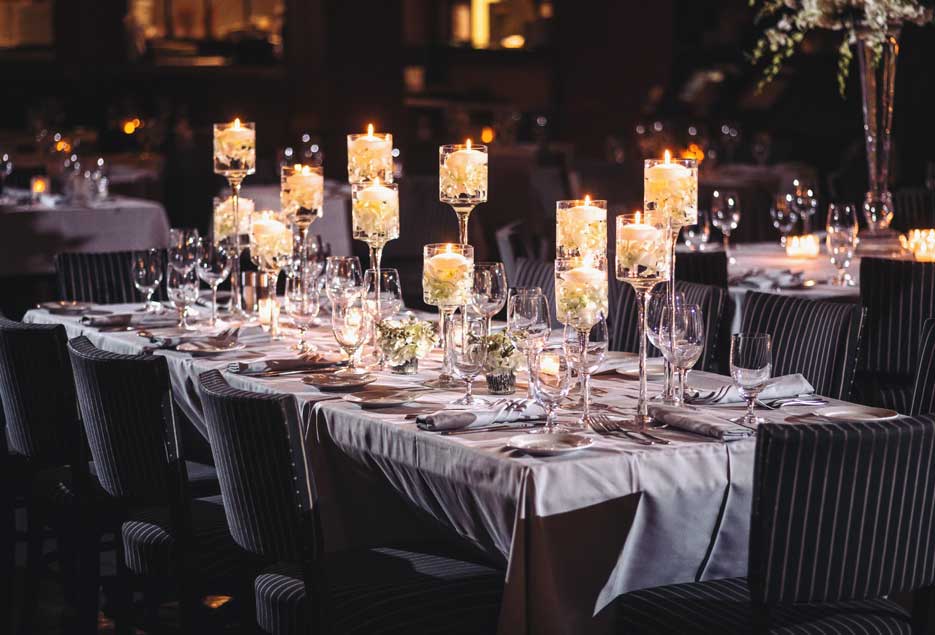 A table setup with various candles on the table with dark navy blue pinstripes accent chairs. 