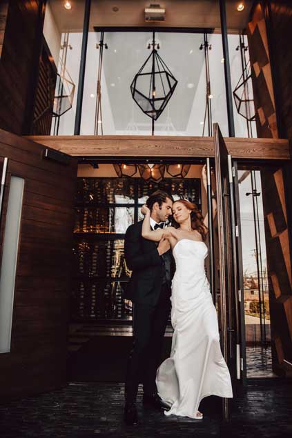 Bride holding the grooms face while standing outside the entrance way of One10. 