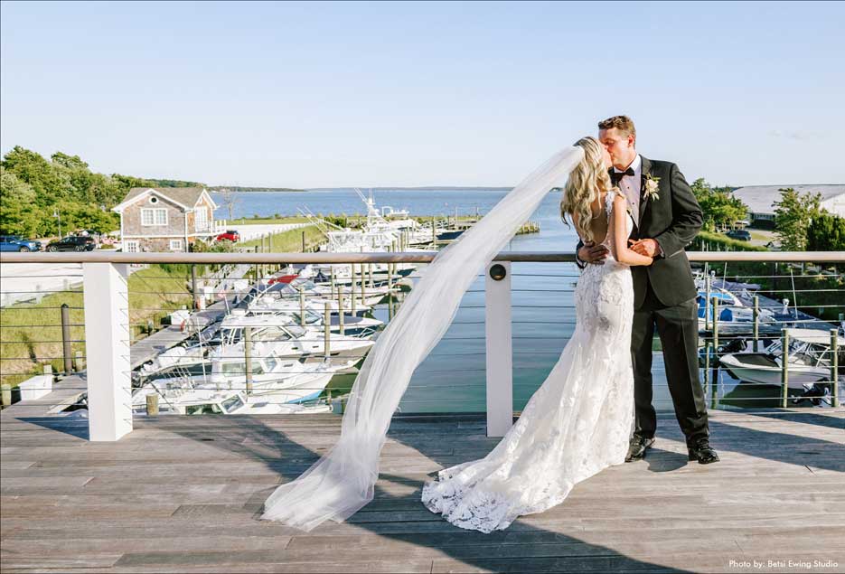 A bride kissing her groom on the deck of the Peconic Bay Yacht Club overlooking the bay. 