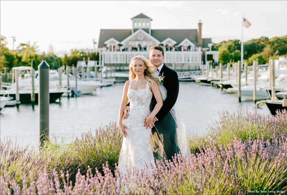 Wedding couple outside surrounded by flowers with the Peconic Bay Yacht Club in the background. 