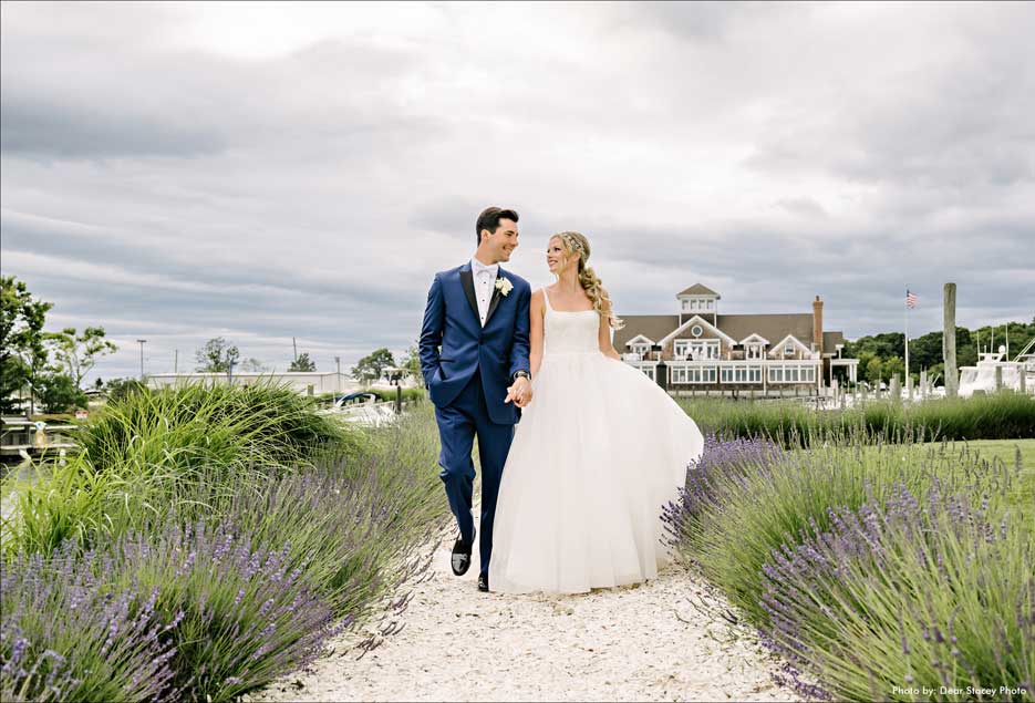 Bride and groom holding hands walking down a stone path surrounding by lavender plants