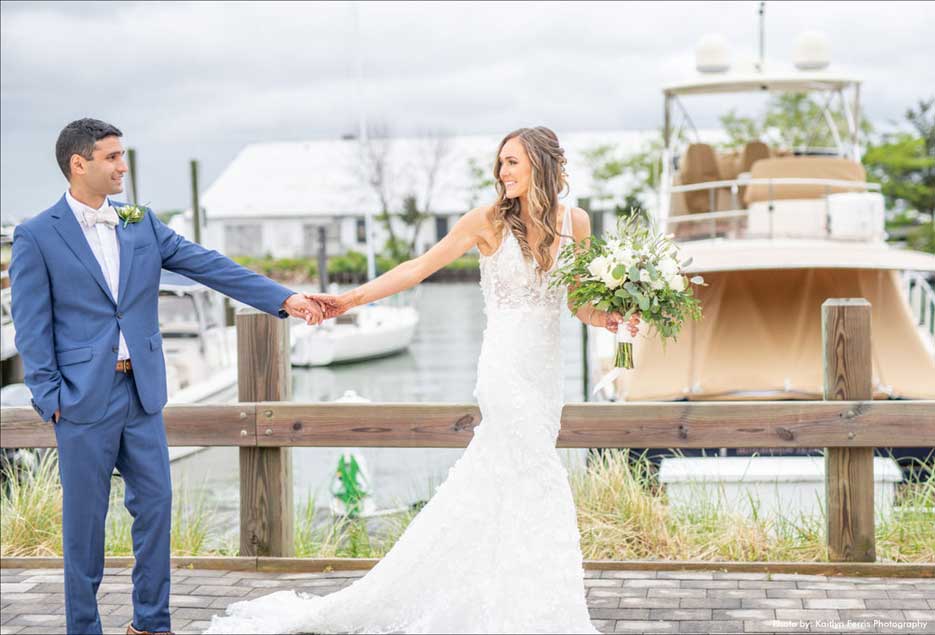 Groom and bride standing by the water with a boat in the background. 