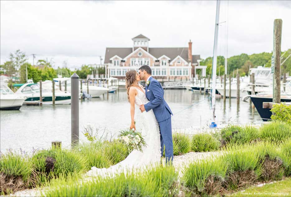 Bride holding her flowers while kissing her groom outside in front of the Peconic Bay Yacht Club. 