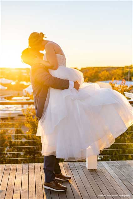 Grooms lifts bride up giving her a kiss with the sunset in the background. 
