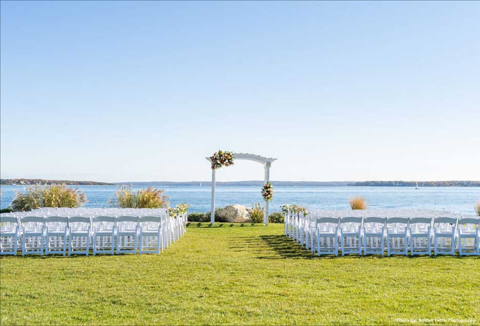 Outdoor wedding ceremony setup with white chairs with the bay as its backdrop. 