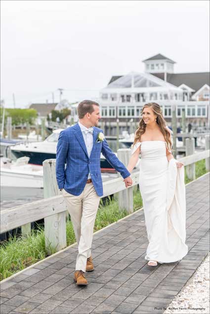Groom holding the brides hand as they walk along the water. 