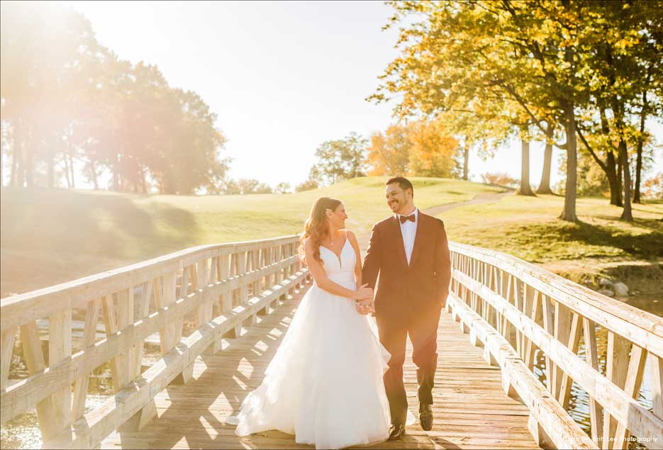 Wedding couple hold hands while walking over the bridge on the gold course. 