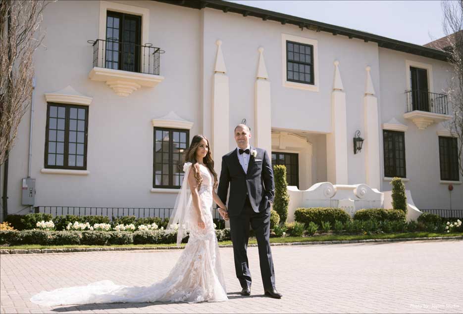 Couple posing for wedding pictures in the front exterior  of the Village Club at Lake Success. 