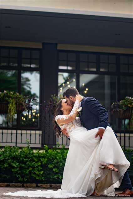 Groom dipping bride back to give her a kiss outside the Village Club at Lake Success. 