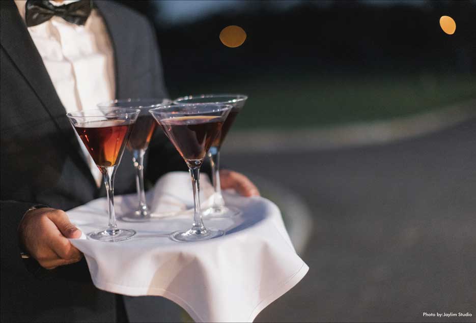 Waiter holding a tray of filled wine glasses for guests at Village Club at Lake Success. 