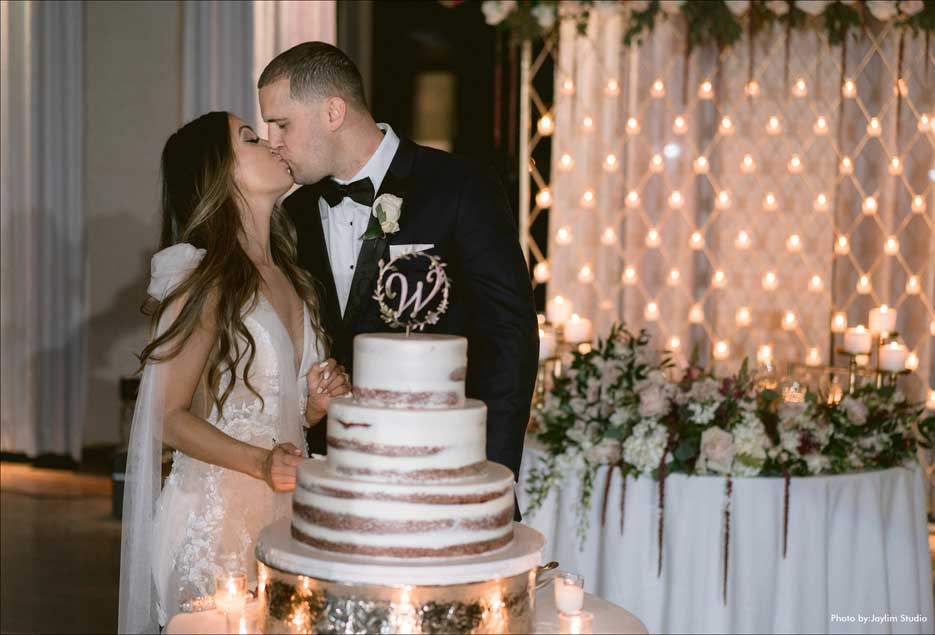 Couple kissing in back of their beautiful white wedding cake.