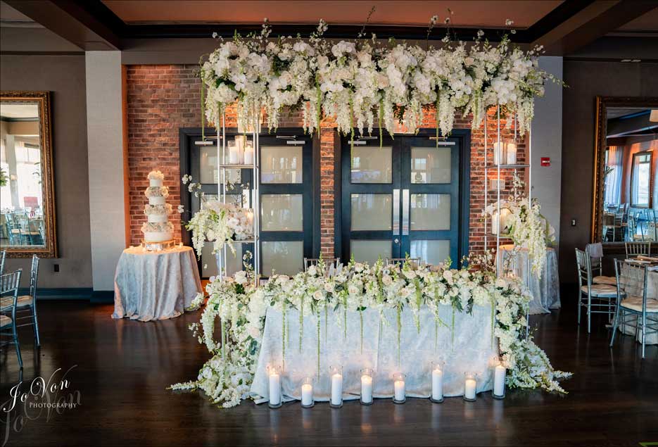 Couples wedding table beautifully decorated with white flowers on table and a white flower arch abov