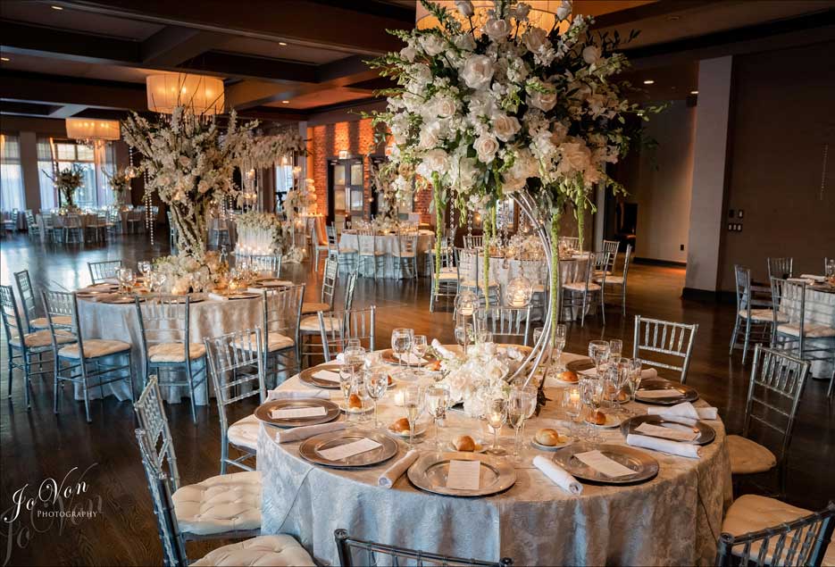 Wedding room setup with beautiful tall white flower centerpieces on each table. 