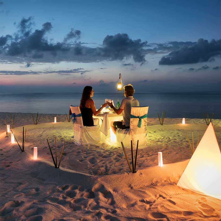 A couple having a romantic dinner on the beach surrounded by candles. 